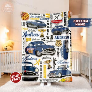 Pode incluir: Um cobertor de bebê branco com um design temático de Carros em azul e amarelo. O cobertor apresenta várias imagens do personagem 'Doc Hudson' do filme Carros. O nome 'Andrew' é repetido ao longo do design.