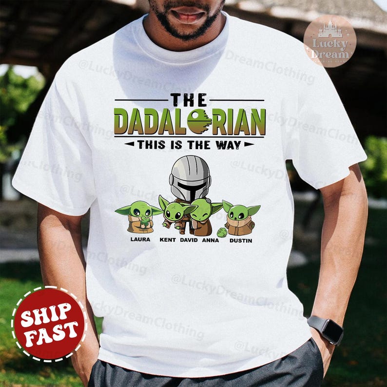 May include: White t-shirt with a green and black graphic of a Mandalorian and four Baby Yodas. The text "The Dadalorian - This is the Way" is above the characters. The names Laura, Kent, David, Anna, and Dustin are below the characters.