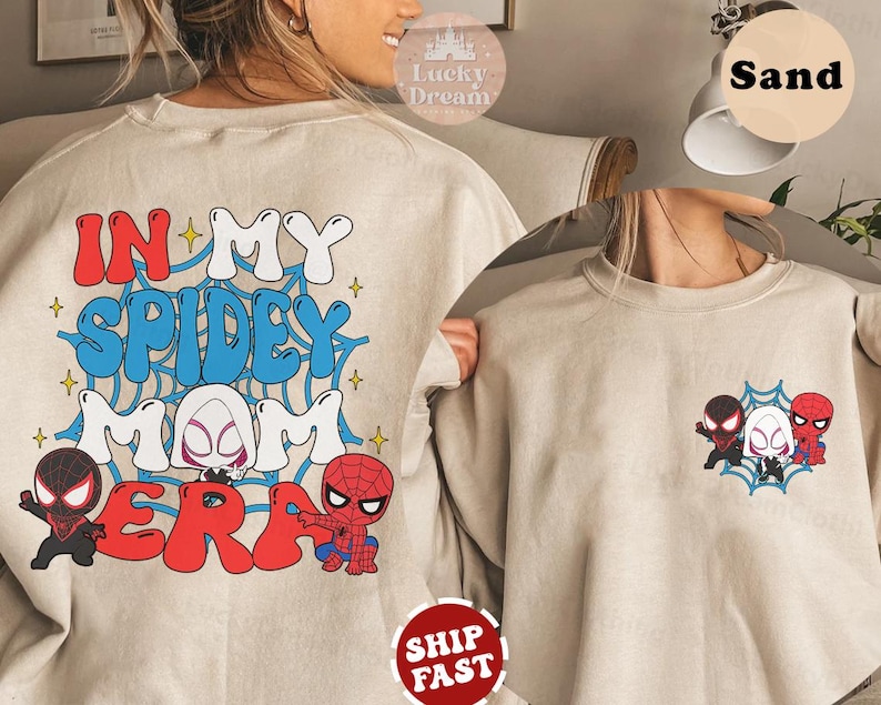 May include: A beige sweatshirt with the text "In My Spidey Mom Era" in red, blue, and white lettering. The sweatshirt features a graphic of Spider-Man characters, including Spider-Man, Spider-Gwen, and Miles Morales.
