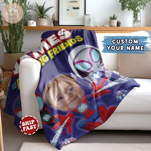 Puede incluir: Una manta personalizada con la cara de un ni&ntilde;o integrada en un dise&ntilde;o de Spider-Man. La manta, en tonos morados, muestra el texto "MES IG FRIENDS" y "CUSTOM YOUR NAME". Se muestra sobre un sof&aacute; blanco.