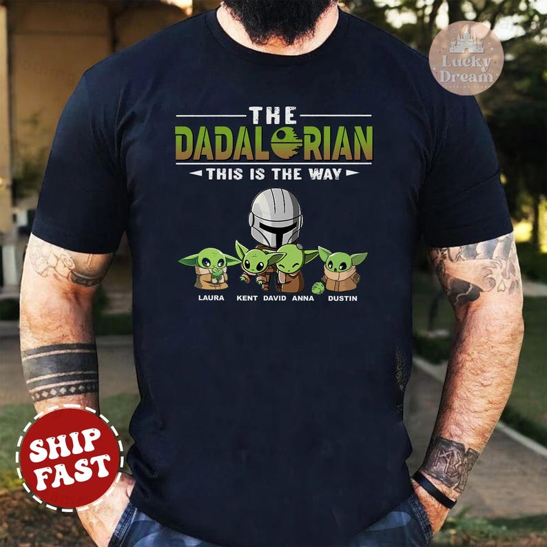 May include: A black t-shirt with a graphic of a Mandalorian character and four Baby Yoda characters. The text "The Dadalorian - This is the Way" is printed on the shirt. The names Laura, Kent, David, Anna, and Dustin are printed below the characters.