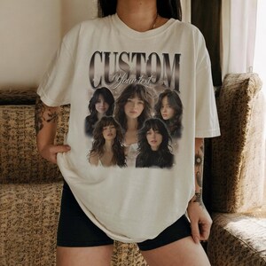 May include: Cream-colored t-shirt featuring the word "CUSTOM" above a graphic of five women. The text "Your text" is below the word "CUSTOM". The women have long hair and are in various poses.