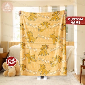 May include: A yellow fleece blanket with a repeating pattern of a cartoon lion cub and the name "SARAH".