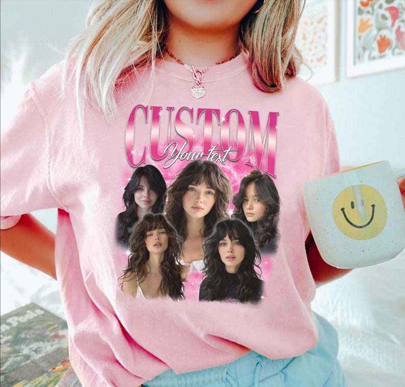 May include: Pink sweatshirt with a graphic design featuring the word "CUSTOM" in a pink gradient font, with the words "Your text" below. The design includes five images of a woman with long hair. A white mug with a yellow smiley face is held in the hand.