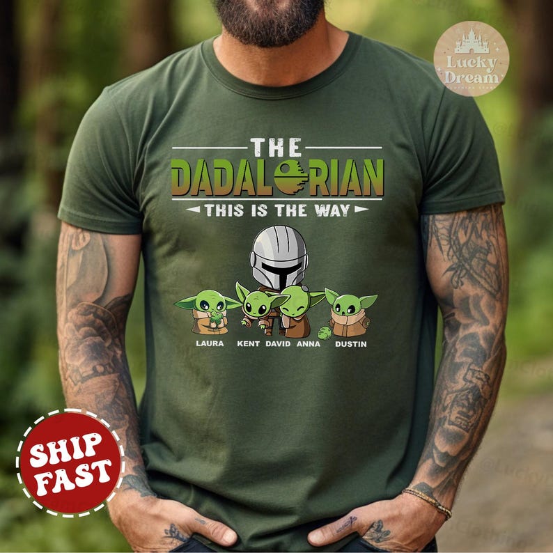 May include: Green t-shirt with a Star Wars themed design featuring a Mandalorian and four Baby Yoda characters. The text reads "The Dadalorian This is the Way" with the names Laura, Kent, David, Anna, and Dustin below the characters.