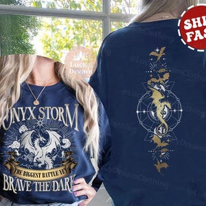 K&ouml;nnte beinhalten: Ein marineblauer Sweatshirt mit einem wei&szlig;en Drachen-Motiv und dem Text "Onyx Storm The Biggest Battle Yet Brave The Dark". Die R&uuml;ckseite des Sweatshirts zeigt ein goldenes Drachen-Motiv mit einem geometrischen Design.