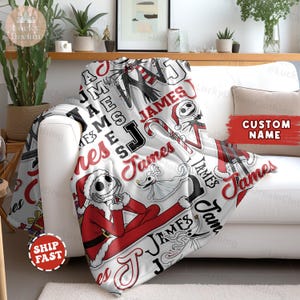 Puede incluir: Una manta blanca con un dise&ntilde;o rojo y negro, que incluye el nombre "James" e ilustraciones de un personaje con un disfraz de Pap&aacute; Noel. La manta est&aacute; sobre un sof&aacute; blanco. Las palabras "Custom Name" son visibles.