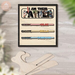 K&ouml;nnte beinhalten: Gerahmtes Star Wars-Kunstwerk mit dem Text "I AM THEIR FATHER" und Charakterillustrationen. Darunter sind Lichtschwert-Designs mit den Namen "CHLOE", "BELLA" und "DONOVAN". Das Kunstwerk befindet sich auf einem hellen Hintergrund.