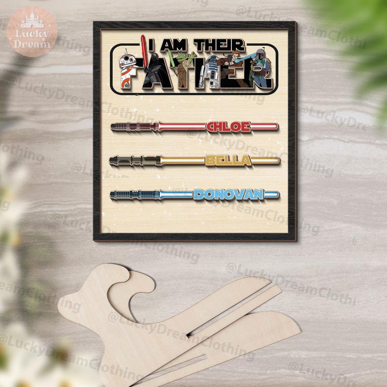 K&ouml;nnte beinhalten: Gerahmtes Star Wars-Kunstwerk mit dem Text "I AM THEIR FATHER" und Charakterillustrationen. Darunter sind Lichtschwert-Designs mit den Namen "CHLOE", "BELLA" und "DONOVAN". Das Kunstwerk befindet sich auf einem hellen Hintergrund.