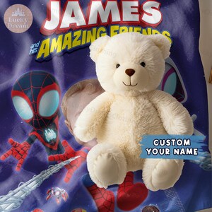 Puede incluir: Un oso de peluche color crema est&aacute; sobre una manta azul con el texto "JAMES and his AMAZING FRIENDS". La manta presenta ilustraciones de Spider-Man y las palabras "CUSTOM YOUR NAME".