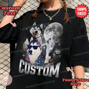 May include: Black t-shirt with a graphic of three husky dogs howling at the moon. The text "CUSTOM" is printed in silver on the shirt. The shirt is available for customization with a picture and text.
