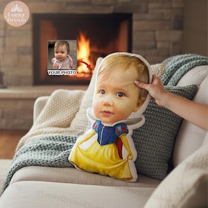 May include: A custom pillow featuring a baby's face, designed to resemble Snow White. The pillow has a yellow dress with blue and red accents. The words "YOUR PHOTO" are visible in the background.