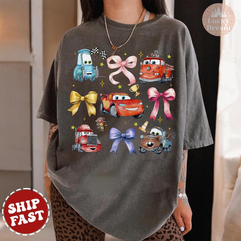 May include: A gray t-shirt with a cartoon image of cars from the Disney Pixar movie Cars. The cars are surrounded by colorful bows. The shirt has a distressed look.