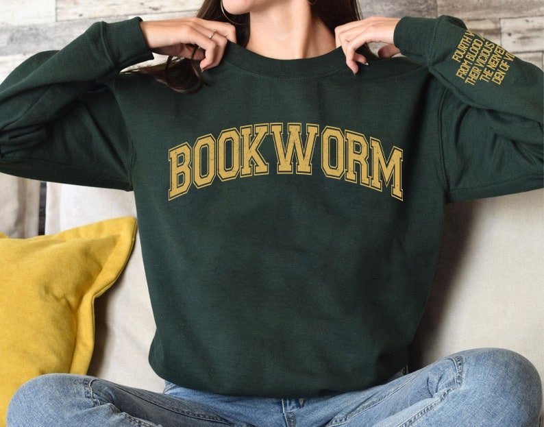 Pode incluir: Uma camisa de moletom verde escura com a palavra "BOOKWORM" impressa em dourado na frente. As mangas t&ecirc;m o texto "FOURTH FROM THE BLOOD THEY WROTE THE NEW RULES OF THE UNIVERSE" impresso em dourado.