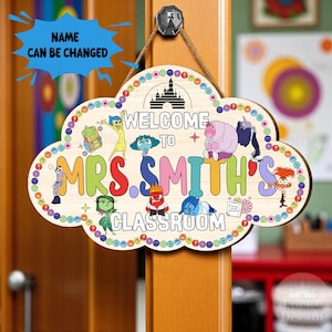 May include: A wooden classroom sign in the shape of a cloud, featuring the text "WELCOME TO MRS. SMITH'S CLASSROOM" with colorful cartoon characters. The sign has a rope for hanging and a black hook.