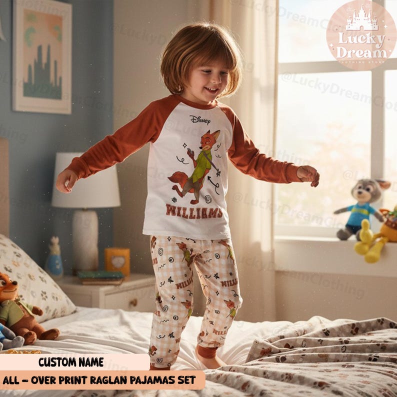 Peut inclure: Ensemble de pyjamas pour enfant avec un haut blanc et des manches marron, orn&eacute; d'un dessin de renard de dessin anim&eacute;. Le pantalon assorti pr&eacute;sente un motif r&eacute;p&eacute;t&eacute;. Le nom "WILLIAMS" est imprim&eacute; en dessous. L'ensemble est &eacute;tiquet&eacute; "ALL-OVER PRINT RAGLAN PAJAMAS SET".