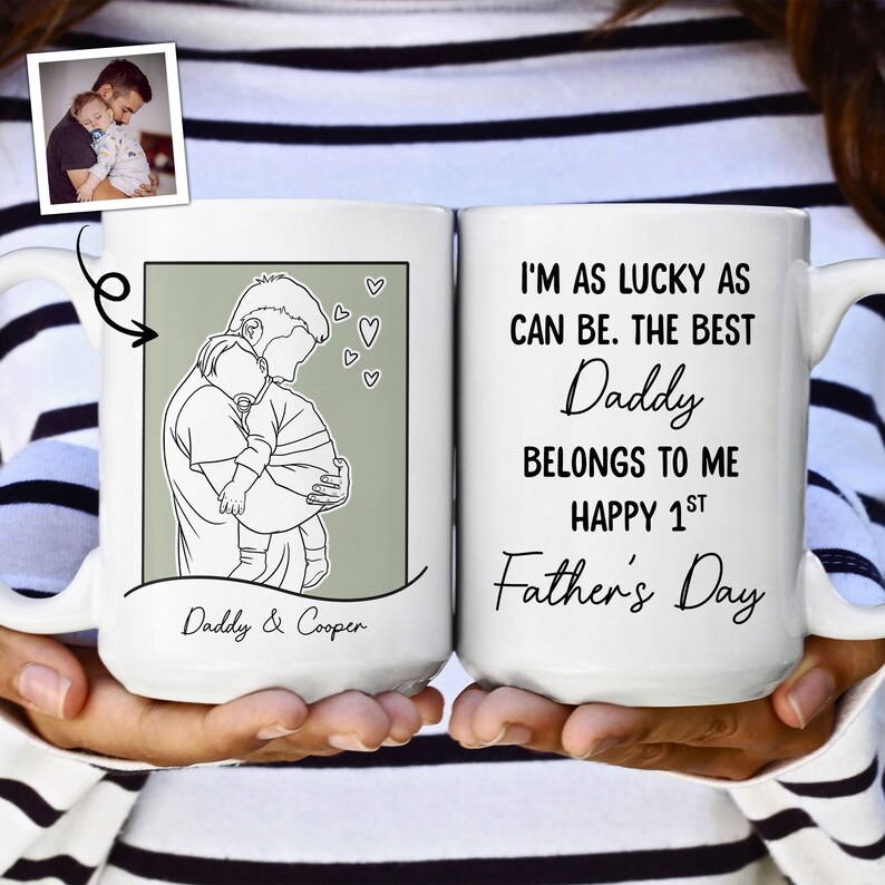 K&ouml;nnte beinhalten: Eine wei&szlig;e Keramiktasse mit einer schwarzen Linienzeichnung eines Vaters, der ein Kind h&auml;lt. Die Tasse tr&auml;gt den Text "Daddy & Cooper" und "I'm as lucky as can be. The best Daddy belongs to me Happy 1st Father's Day".