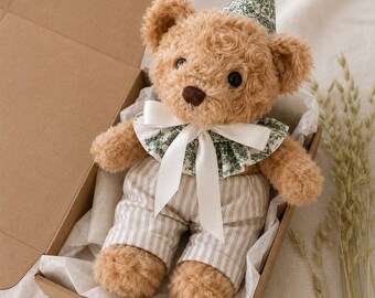 May include: A plush brown teddy bear wearing a party hat and a decorative collar with a white bow. The bear is dressed in striped pants and is presented in a cardboard box with white tissue paper.