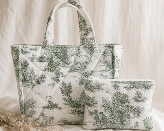 May include: A quilted tote bag and matching pouch set. The bags feature a white background with a green toile pattern depicting a pastoral scene. The tote has a rectangular shape with handles, and the pouch is a smaller, rectangular zippered bag.