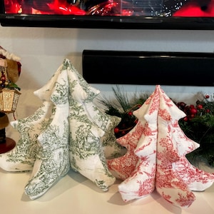 Könnte beinhalten: Drei Weihnachtsbaumdekorationen aus Stoff. Zwei Bäume sind weiß mit einem grünen Toile-de-Jouy-Muster, und einer ist rot mit einem weißen Toile-de-Jouy-Muster. Die Bäume sind auf einer weißen Oberfläche angeordnet, mit Grün im Hintergrund.