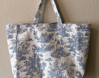 May include: A white tote bag with a blue and white toile pattern. The bag has two handles and is hanging on a hook.