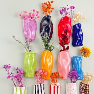 May include: A collection of colorful ceramic vases in various shapes and sizes, each holding dried flowers and greenery. The vases are in shades of pink, green, orange, red, blue, and black, with some featuring striped and dotted patterns. A decorative floral arrangement.