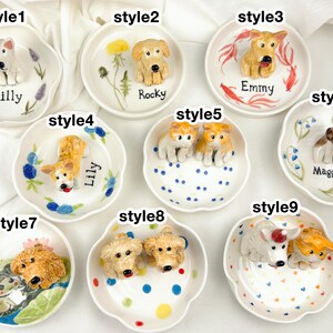 May include: A collection of nine small, white ceramic dishes, each adorned with a 3D dog figurine. The dishes feature various dog breeds and are decorated with floral and dot patterns. Each dish has a dog's name written on it.