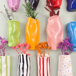 May include: A collection of colorful ceramic vases in various shapes and sizes, some with vertical stripes or polka dots. The vases are filled with dried flowers and greenery, creating a vibrant display. The color palette includes green, orange, pink, and blue.