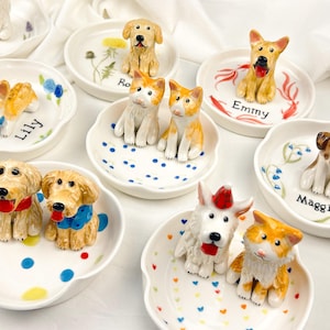 May include: A collection of ceramic dog figurines on small, white, scalloped dishes. Each dish features a different dog breed, with names like "Lily" and "Maggie" written on them. The dishes are decorated with colorful patterns and floral accents.