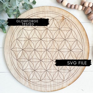 Op de afbeelding: Een ronde houten schijf met een lasergesneden ontwerp van een levensbloempatroon. De schijf heeft de tekst "Glowforge Tested" en "SVG File" erop.