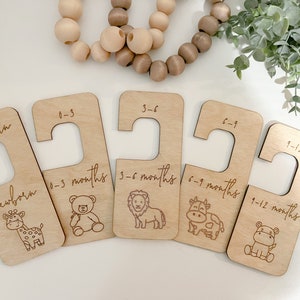 May include: Wooden baby clothes dividers with engraved text and animal illustrations. Sizes include newborn, 0-3 months, 3-6 months, 6-9 months, and 9-12 months. The dividers are made of light-colored wood.