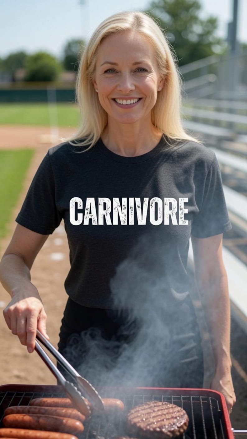 May include: A charcoal grey short-sleeved t-shirt featuring the word CARNIVORE printed in bold white capital letters across the chest. The shirt has a crew neckline and a standard fit, made from a heathered fabric texture.