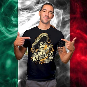 May include: Black t-shirt featuring a cartoon character playing a guitar and wearing a sombrero. The design includes the word "Mexico" in a decorative font, with musical notes and floral accents. The background is a stylized Mexican flag.