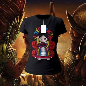 May include: Black t-shirt with a colorful embroidered image of a traditional Mexican doll. The doll is wearing a red, yellow, and green dress with a white blouse and a red bow in her hair.