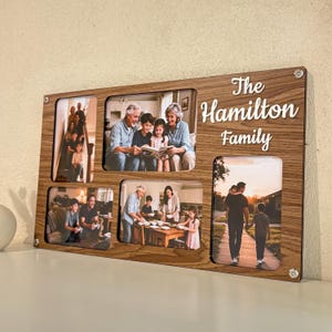 May include: A wooden family photo frame with five rectangular openings, each displaying a different family photo. The frame is engraved with the words "The Hamilton Family" in a cursive font. The frame is made of wood and has a light brown color.