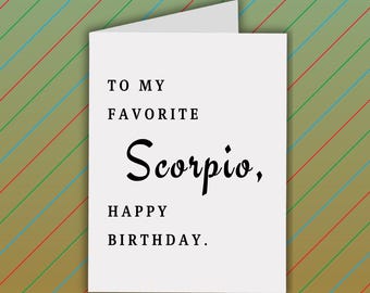Könnte beinhalten: Eine weiße Geburtstagskarte mit dem Text "TO MY FAVORITE Scorpio, HAPPY BIRTHDAY." Die Karte ist gefaltet und vor einem Hintergrund mit diagonalen Streifen in Grün, Blau und Rot platziert.