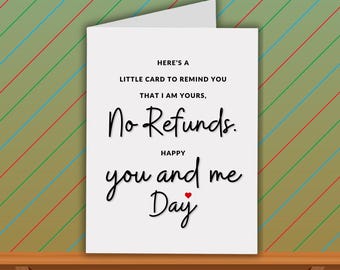 May include: A white greeting card with the text "HERE'S A LITTLE CARD TO REMIND YOU THAT I AM YOURS, No Refunds. HAPPY you and me Day" in black script. A small red heart is below the words "you and me Day". The card is on a wooden surface.