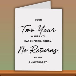 Pode incluir: Cart&atilde;o branco com texto preto: "YOUR Two-Year WARRANTY HAS EXPIRED. SORRY, No Returns. HAPPY ANNIVERSARY." O cart&atilde;o est&aacute; sobre uma superf&iacute;cie de madeira.