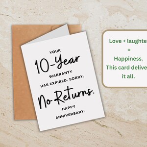 Op de afbeelding: Een witte jubileumkaart met zwarte tekst met de tekst "YOUR 10-Year WARRANTY HAS EXPIRED. SORRY, No Returns. HAPPY ANNIVERSARY." Achter de kaart zit een bruine envelop. Een groene doos bevat de tekst "Love + laughter = Happiness. This card delivers it all."