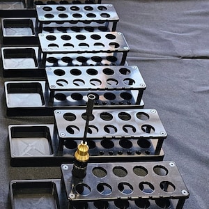 May include: A set of black plastic storage organizers with multiple compartments. The organizers are stacked on top of each other and have a small tray on the bottom. A black and gold tool is in the top organizer.