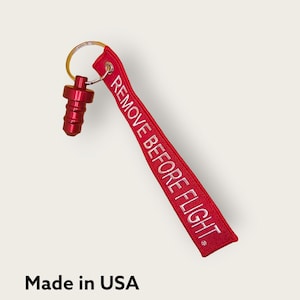 May include: Red keychain with a metal ring and a red plastic pull tab. The keychain has a white embroidered label that says "REMOVE BEFORE FLIGHT".