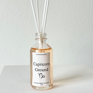 May include: A clear glass bottle of Capricorn Ground handmade reed diffuser oil with white reeds. The label features the text "TANSAGAMORE", "Capricorn Ground", and the Capricorn symbol. The bottle contains 2 oz of oil.