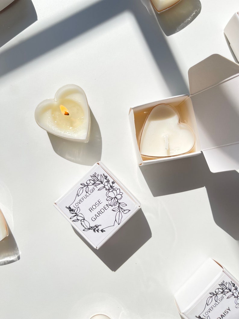 May include: Three white heart-shaped candles in boxes. The boxes are white with black text and floral designs. The text on the boxes reads "Lovefullgift Rose Garden" and "Lovefullgift Daisy".