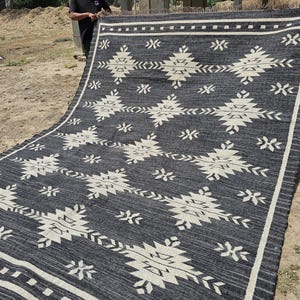 May include: Black and white geometric patterned rug with a fringe border. The rug is folded in half and laid out on the ground.