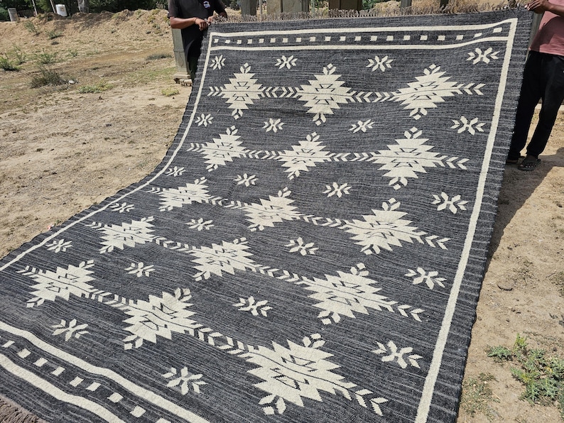 May include: Black and white geometric patterned rug with a fringe border. The rug is folded in half and laid out on the ground.