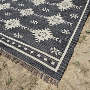 May include: Black and white geometric patterned rug with fringe. The rug has a dark gray background with white geometric shapes.