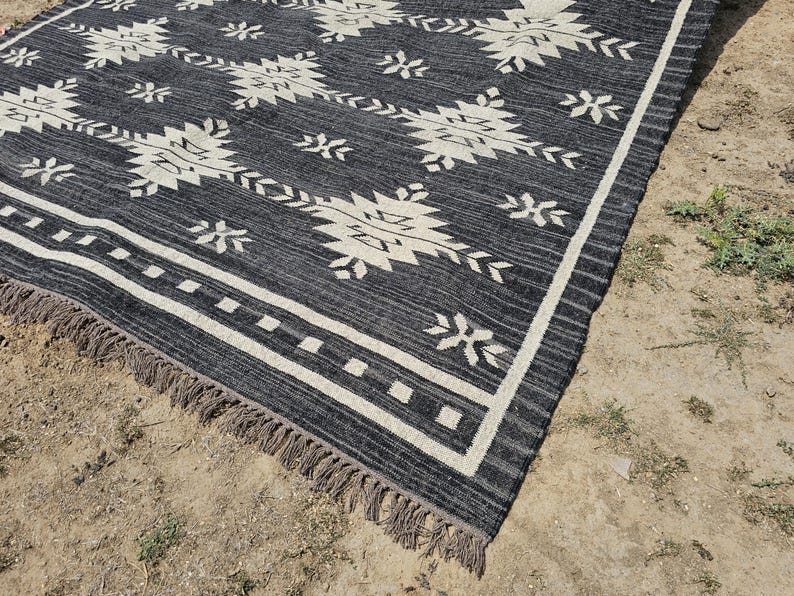 May include: Black and white geometric patterned rug with fringe. The rug has a dark gray background with white geometric shapes.