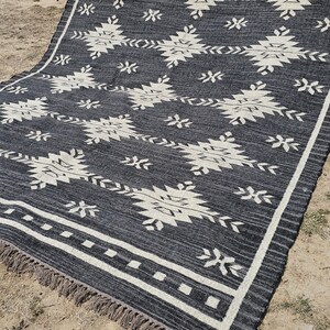 May include: Black and white geometric patterned rug with a fringe border. The rug has a contemporary design with a black background and white geometric shapes.