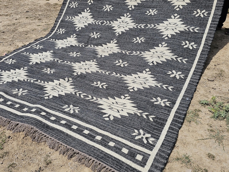 May include: Black and white geometric patterned rug with a fringe border. The rug has a contemporary design with a black background and white geometric shapes.