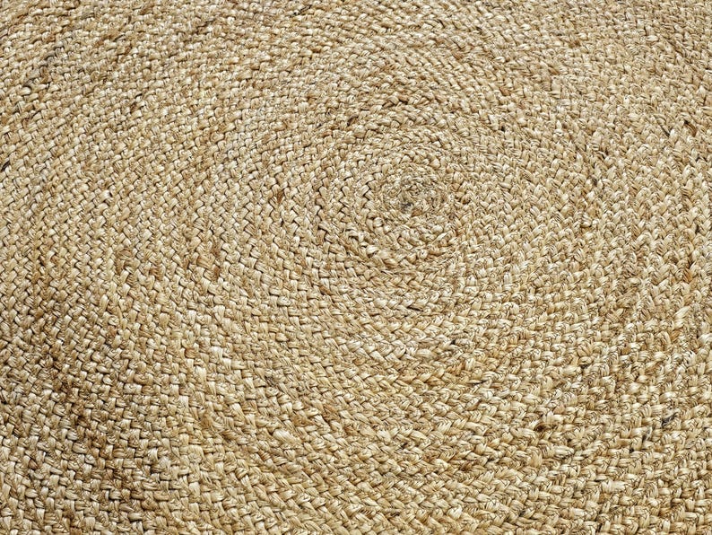 Peut inclure: Gros plan sur un tapis rond en jute. Le tapis en fibre naturelle pr&eacute;sente un motif en spirale, avec des brins &eacute;troitement tiss&eacute;s cr&eacute;ant une surface textur&eacute;e. La palette de couleurs neutres du tapis le rend adapt&eacute; &agrave; divers styles d'int&eacute;rieur.